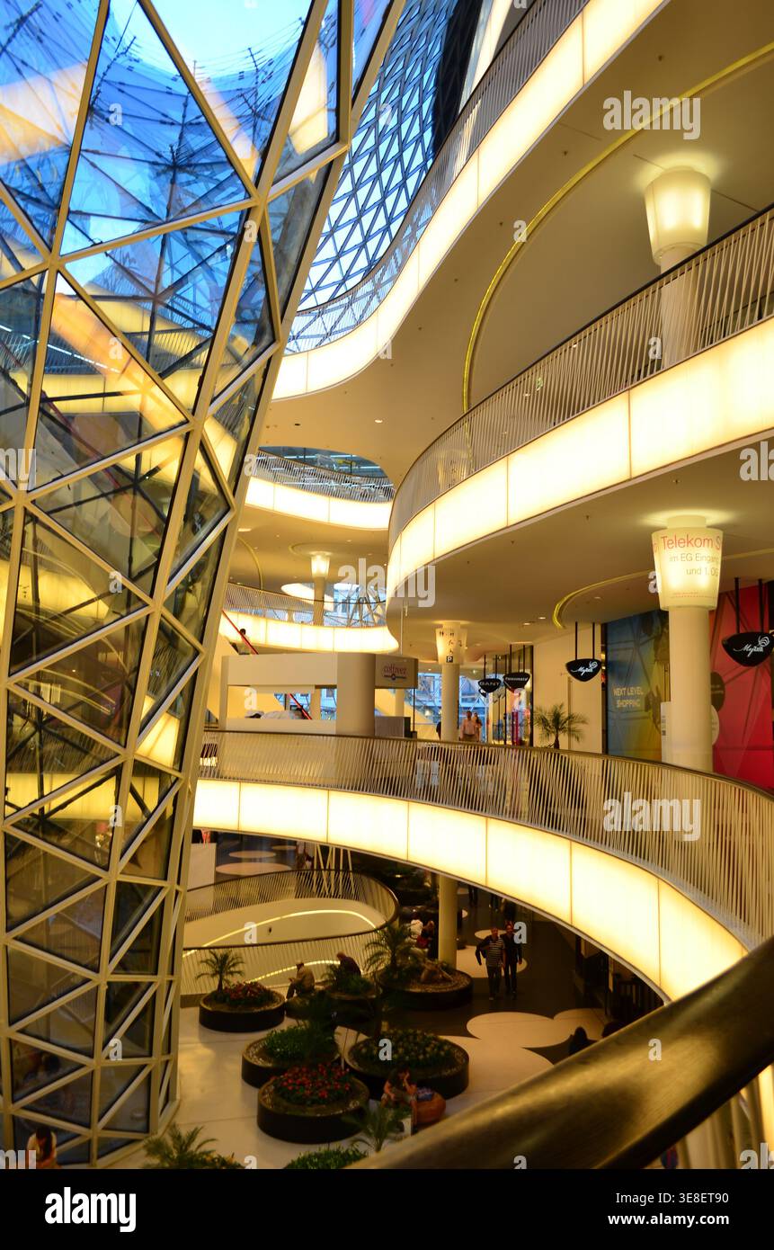 Modern shopping mall interior featuring a striking glass roof and illuminated curved walkways Stock Photo