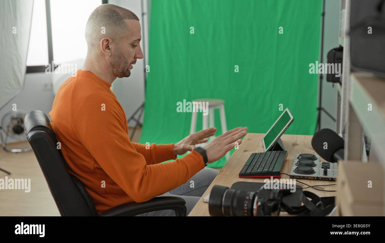 Man photographer pointing at tablet and gesturing with hands at desk in studio, green screen and camera visible; concentration creativity. Stock Photo