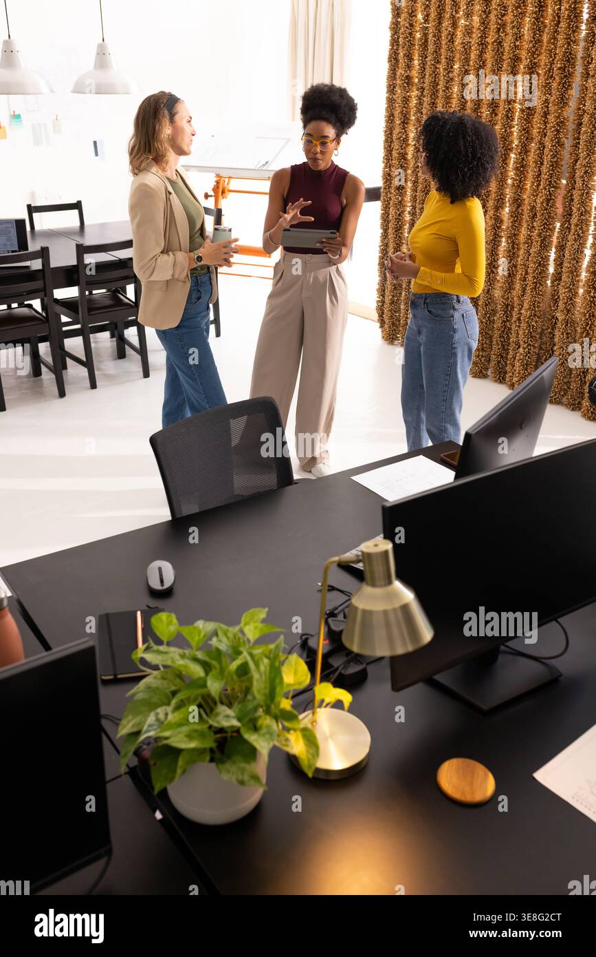 Three women presenting on tablet, collaborating on project in bright open-plan office Stock Photo