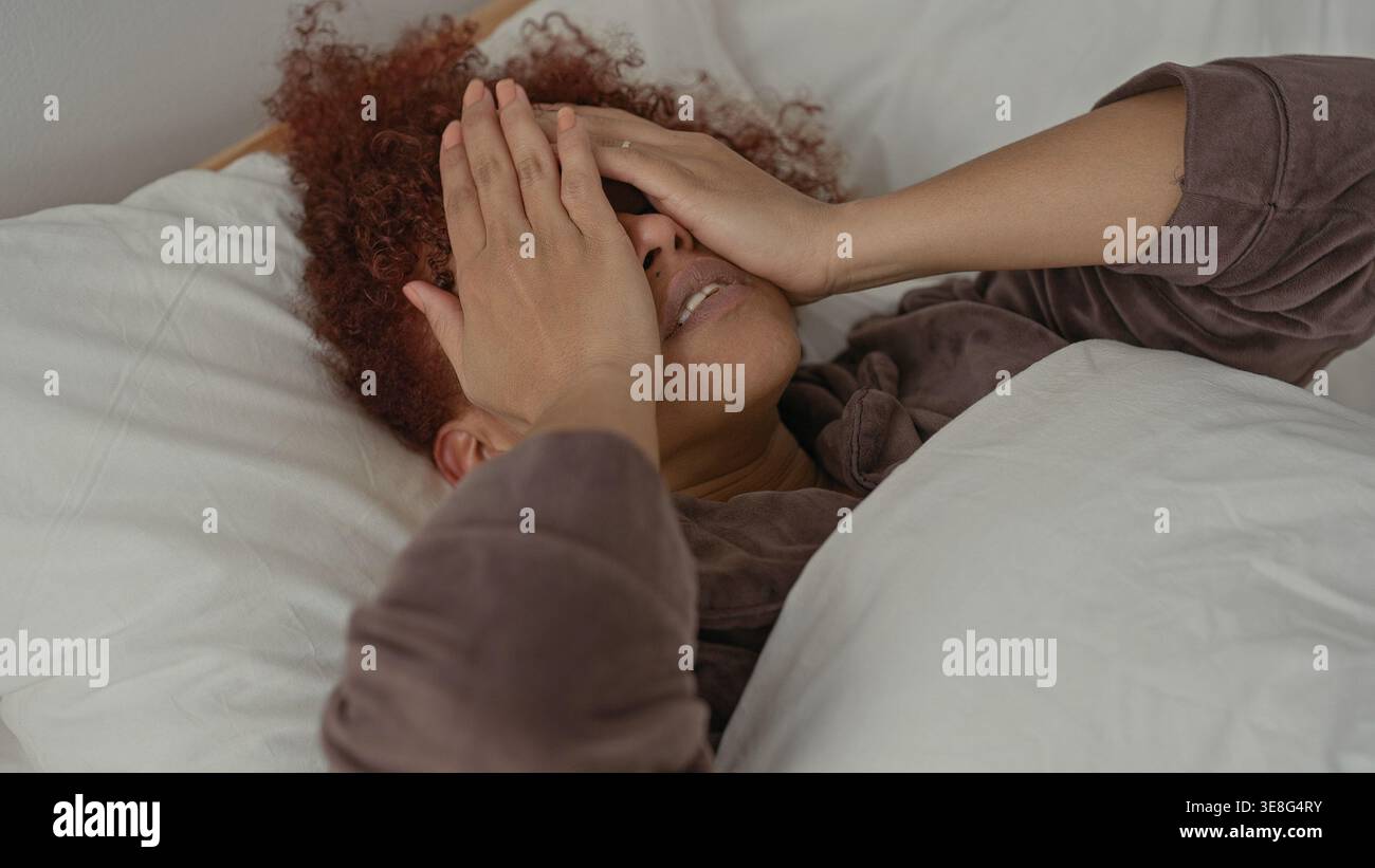 Woman covering face with both hands while lying on bed in studio ...