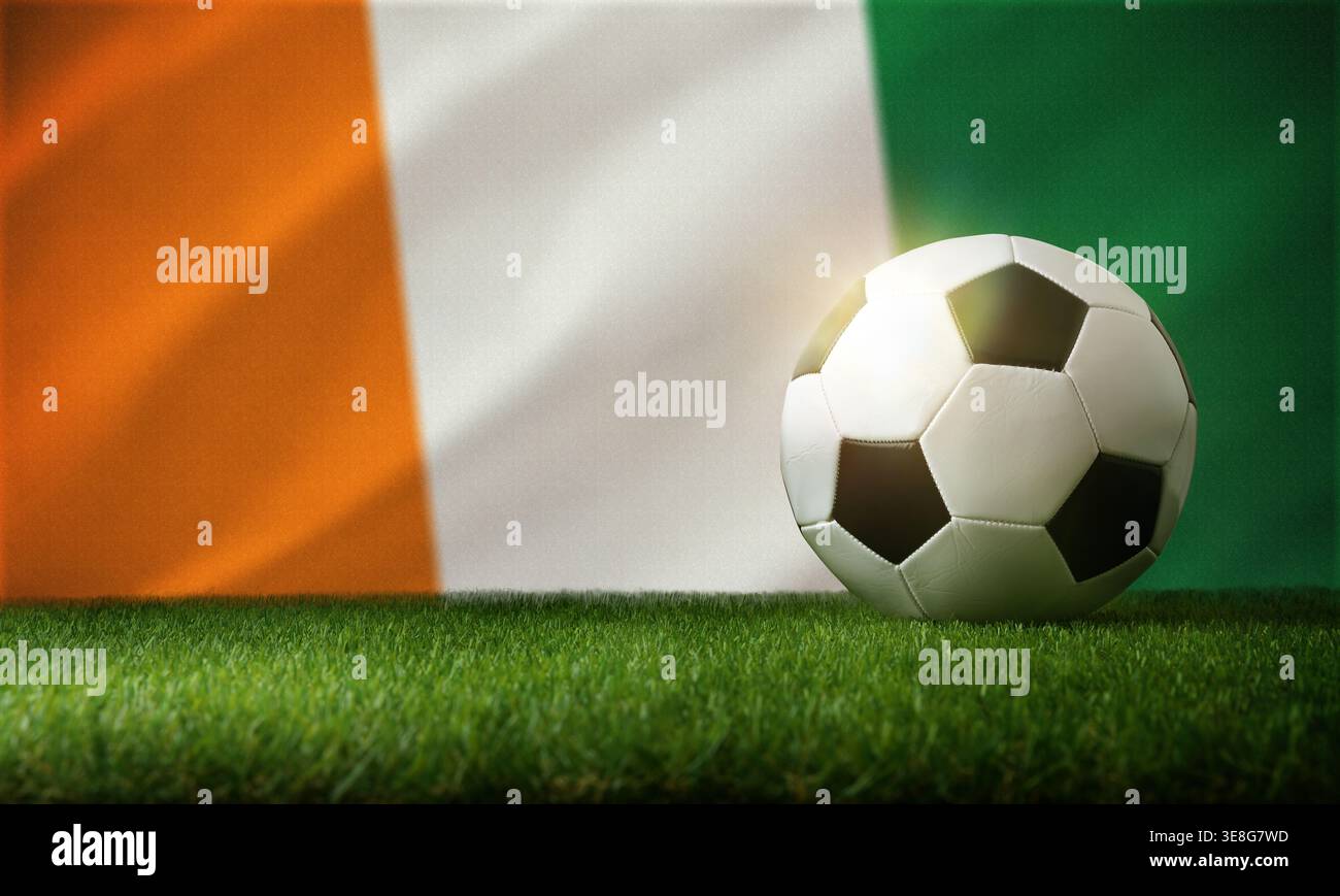 A soccer ball rests on green grass with a blurred Ivory Coast flag in the background, symbolizing sports and national pride. Stock Photo