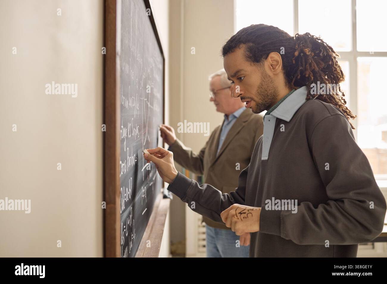 Black Adult Man Solving Equations in Classroom with Senior Teacher Stock Photo