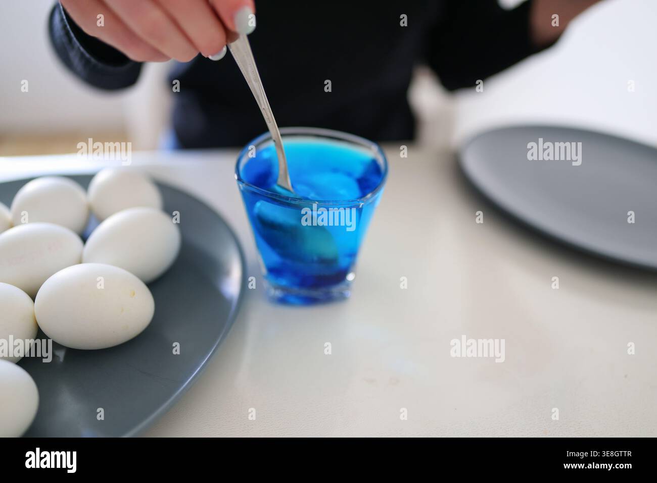 Coloring eggs in vibrant blue, festive preparation and creative kitchen moment. Stock Photo