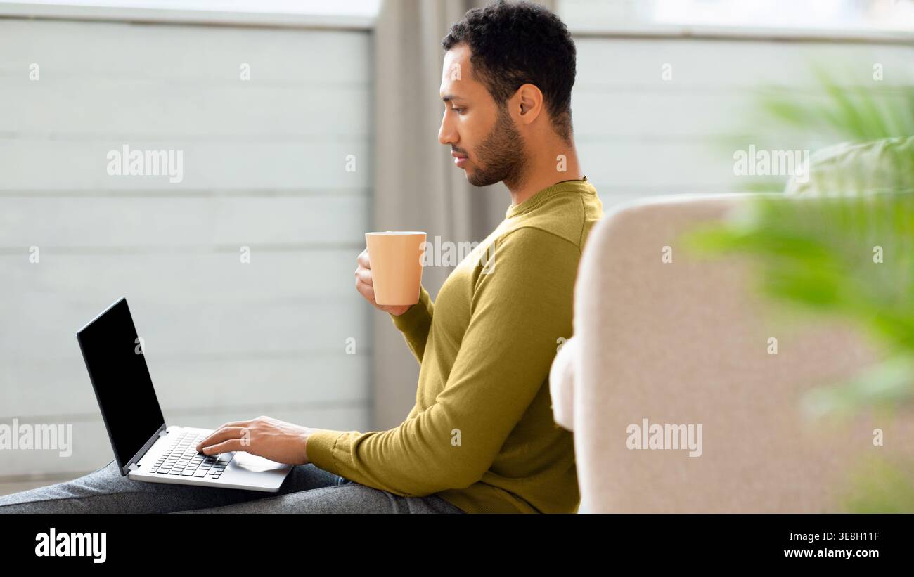 Man Working on Laptop While Sitting on the Floor and Holding a Cup in a Light Room Stock Photo