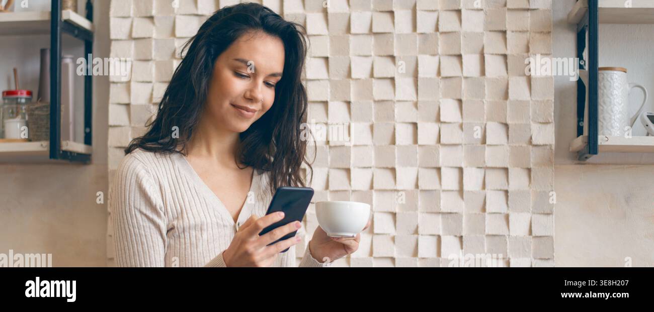 Young Woman Enjoys Coffee While Using Smartphone in a Cafe Setting Stock Photo