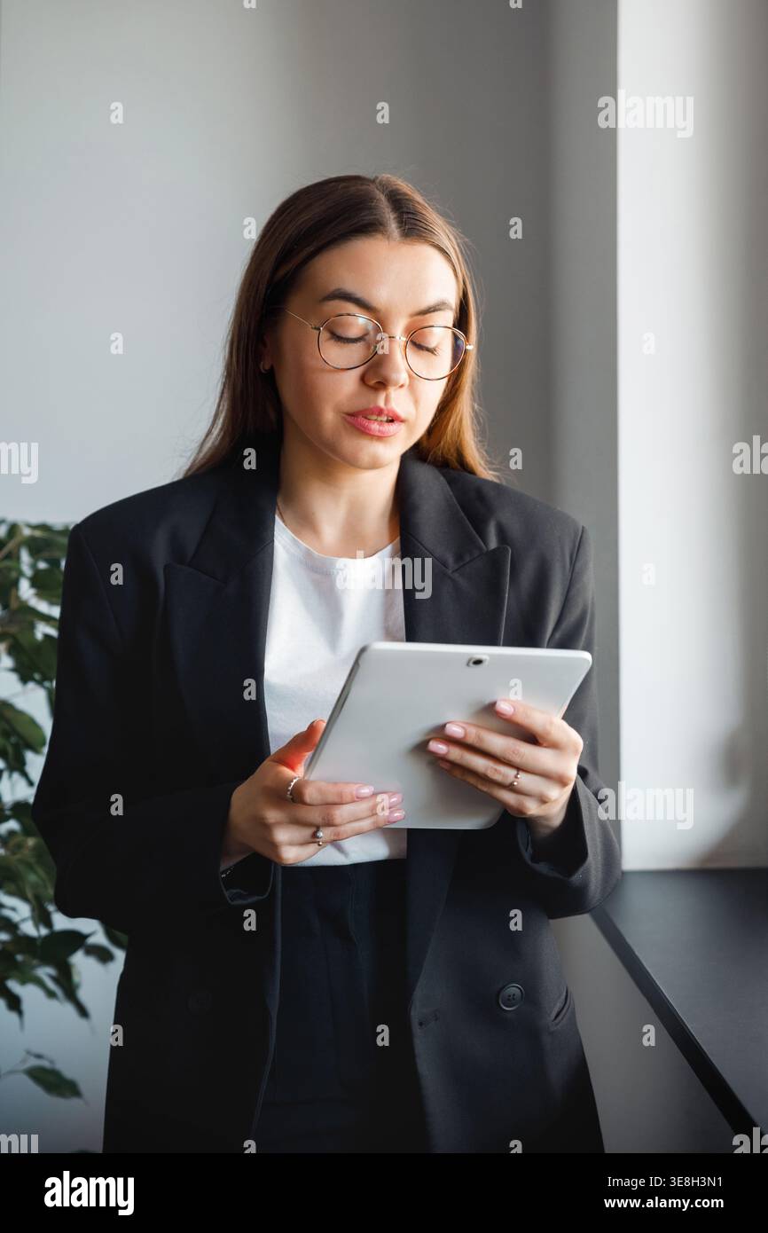 Woman using tablet at office desk. Attractive businesswoman working with digital device. Female professional using technology in modern corporate offi Stock Photo