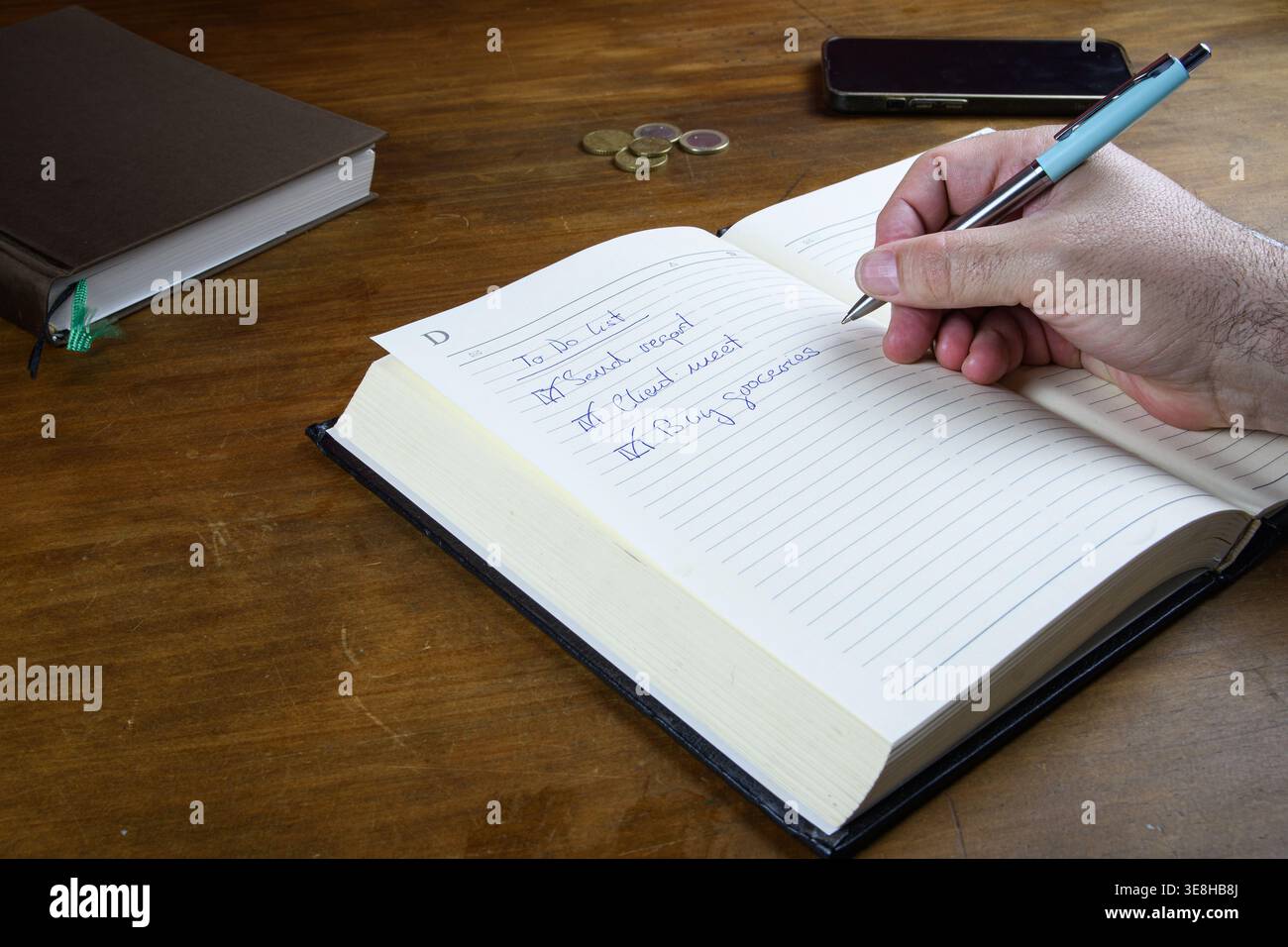 Hand writing a to do list in notebook on wooden desk, home productivity and task management concept. Stock Photo