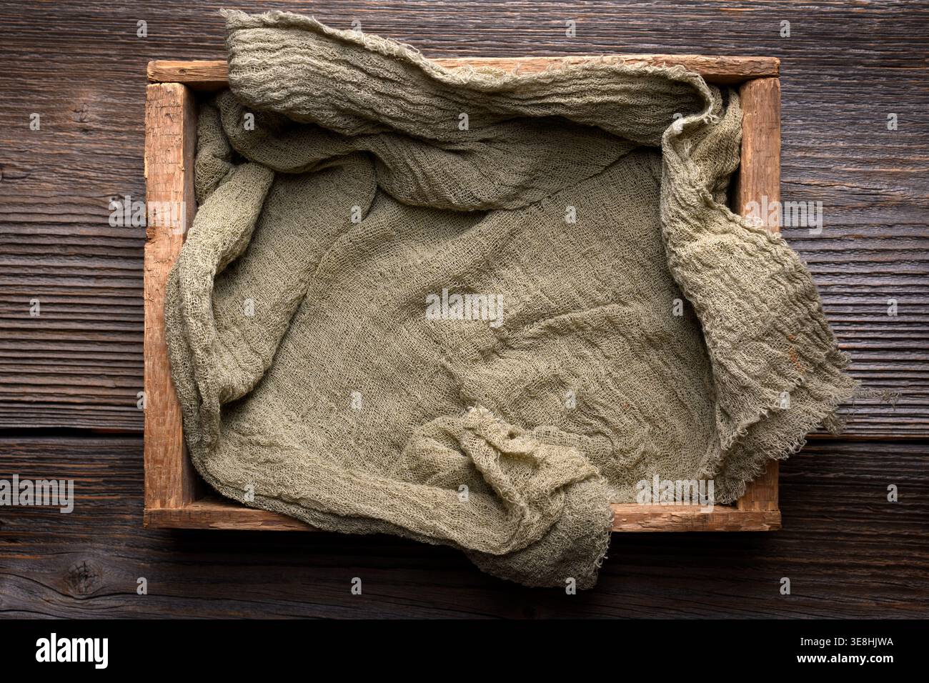 Empty wooden crate with linen cloth on rustic table, top view. Farm container mockup, food styling background Stock Photo