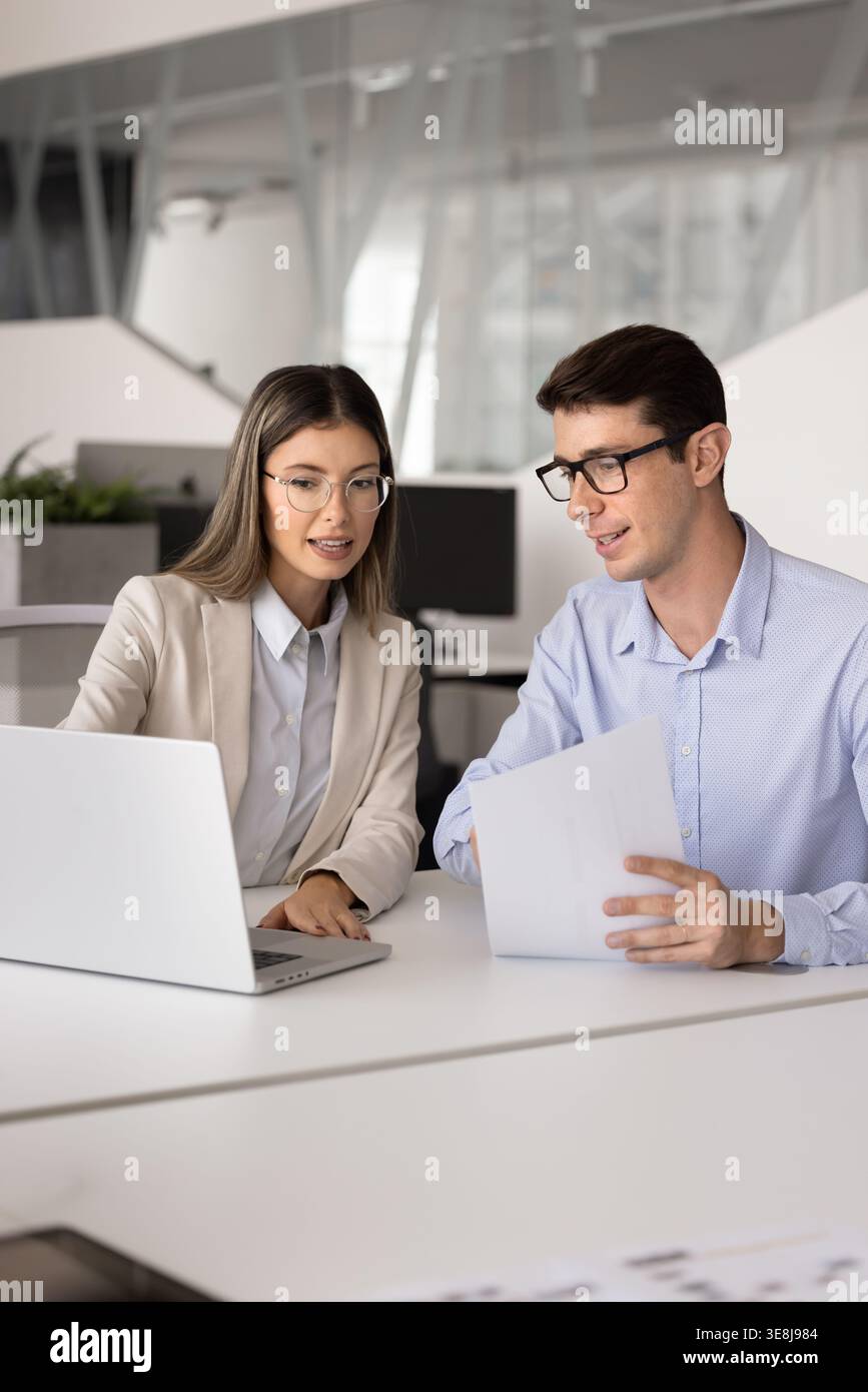 Coworkers discussing project details using laptop and papers Stock Photo