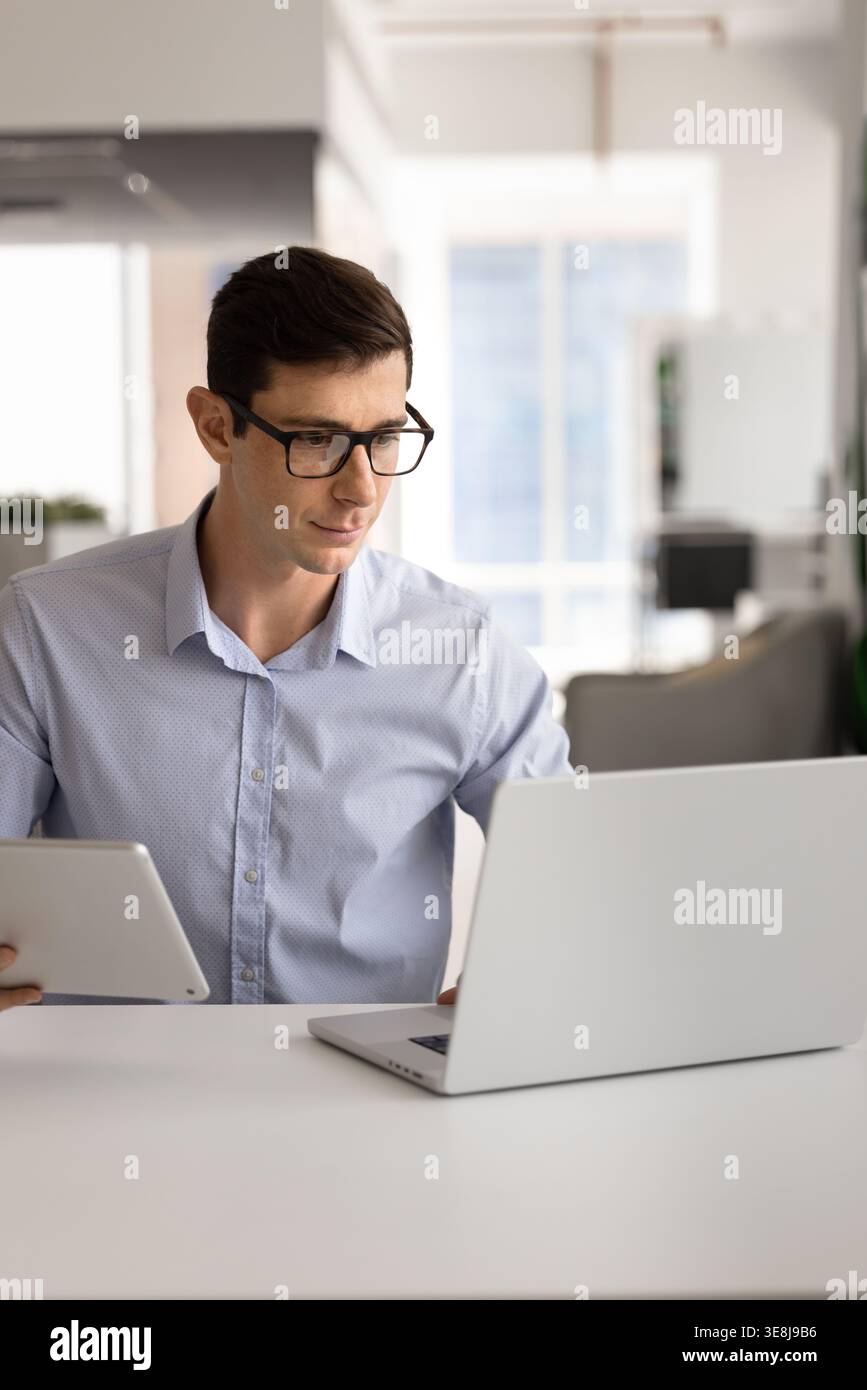 Man using laptop and holding digital tablet in office Stock Photo