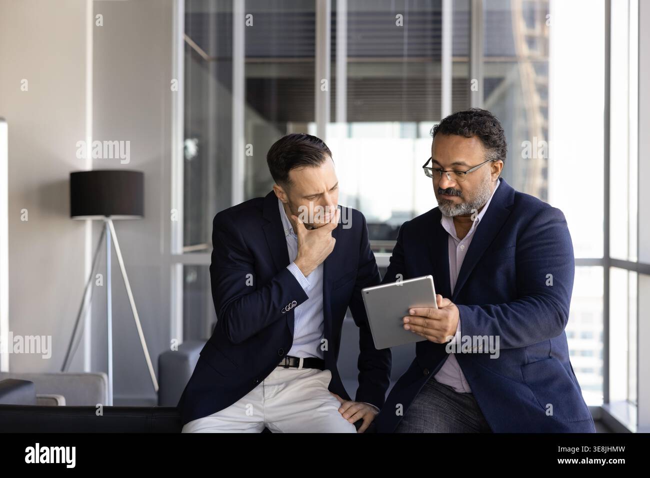 Two businessmen reviewing data, making information analysis on digital tablet Stock Photo