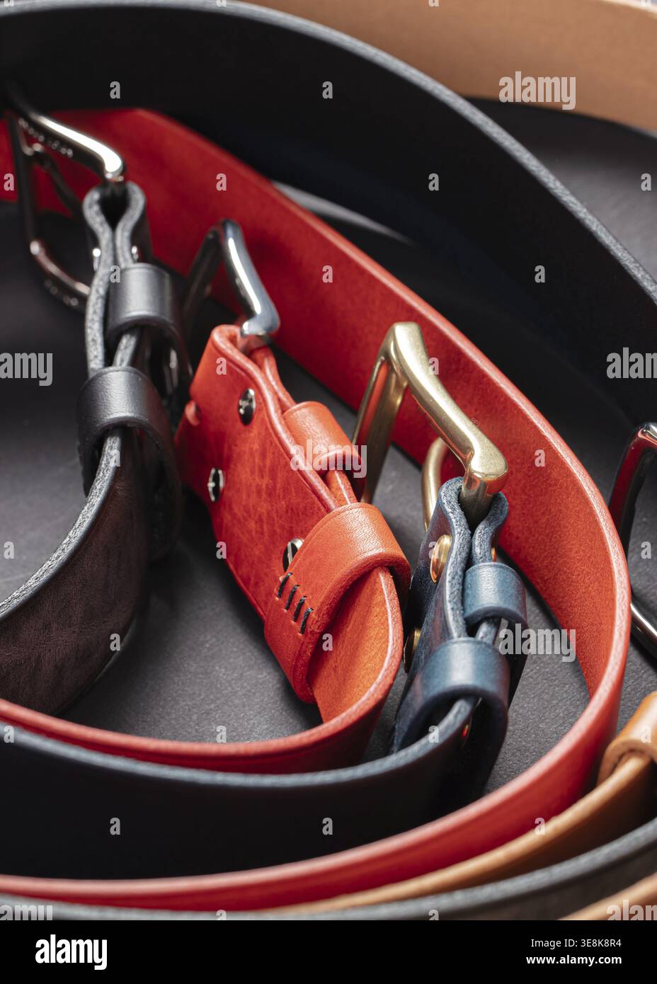 Various leather belts with metal buckles close-up on dark grey background Stock Photo