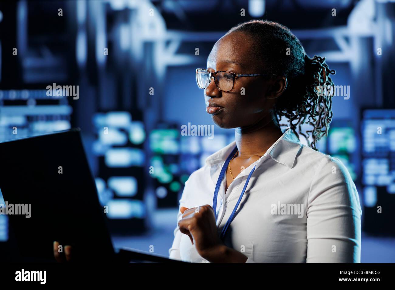 Proficient admin in high tech establishment uses laptop to prevent system overload. Competent expert between server cabinets ensuring enough network bandwidth for smooth operations Stock Photo