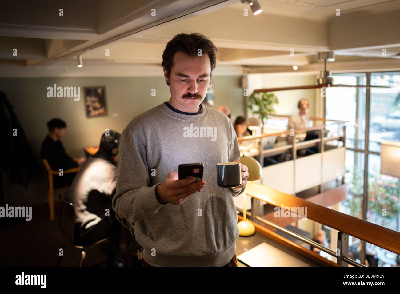 Handsome businessman enjoying coffee and scrolls smartphone after finishing work at co-working cafe. Stock Photo