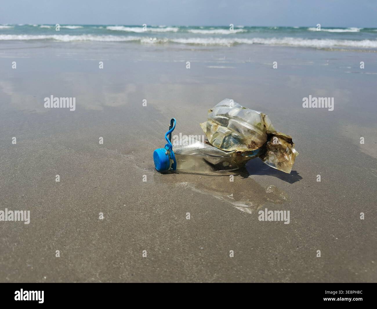 Ocean's Unwanted Guest: A weathered plastic bottle lies stranded on the sandy shore Stock Photo