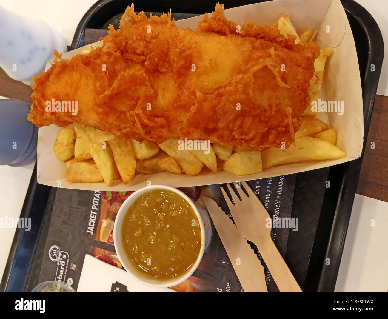 Thick battered fish and chips with curry sauce in a recyclable tray, showing rising costs of a classic British chip shop meal. Stock Photo