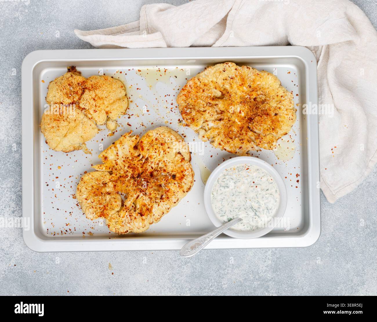 Baked cauliflower steaks with herbs and spices on a baking sheet on a gray concrete background. Mayonnaise sauce with dill, parsley and garlic. Vegan, Stock Photo