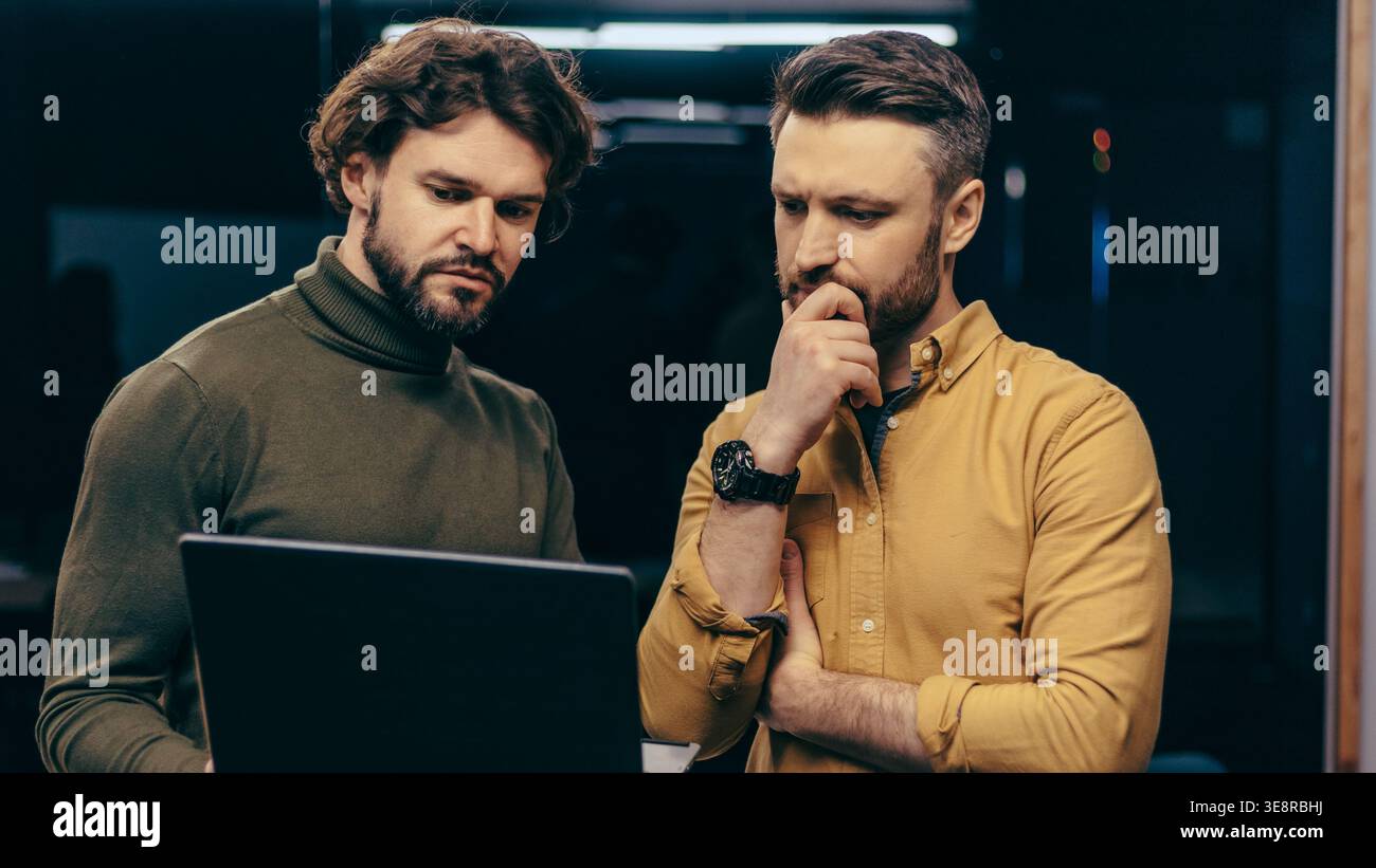 Two Men Focus on a Laptop Screen While Discussing Work in an Office Setting Stock Photo