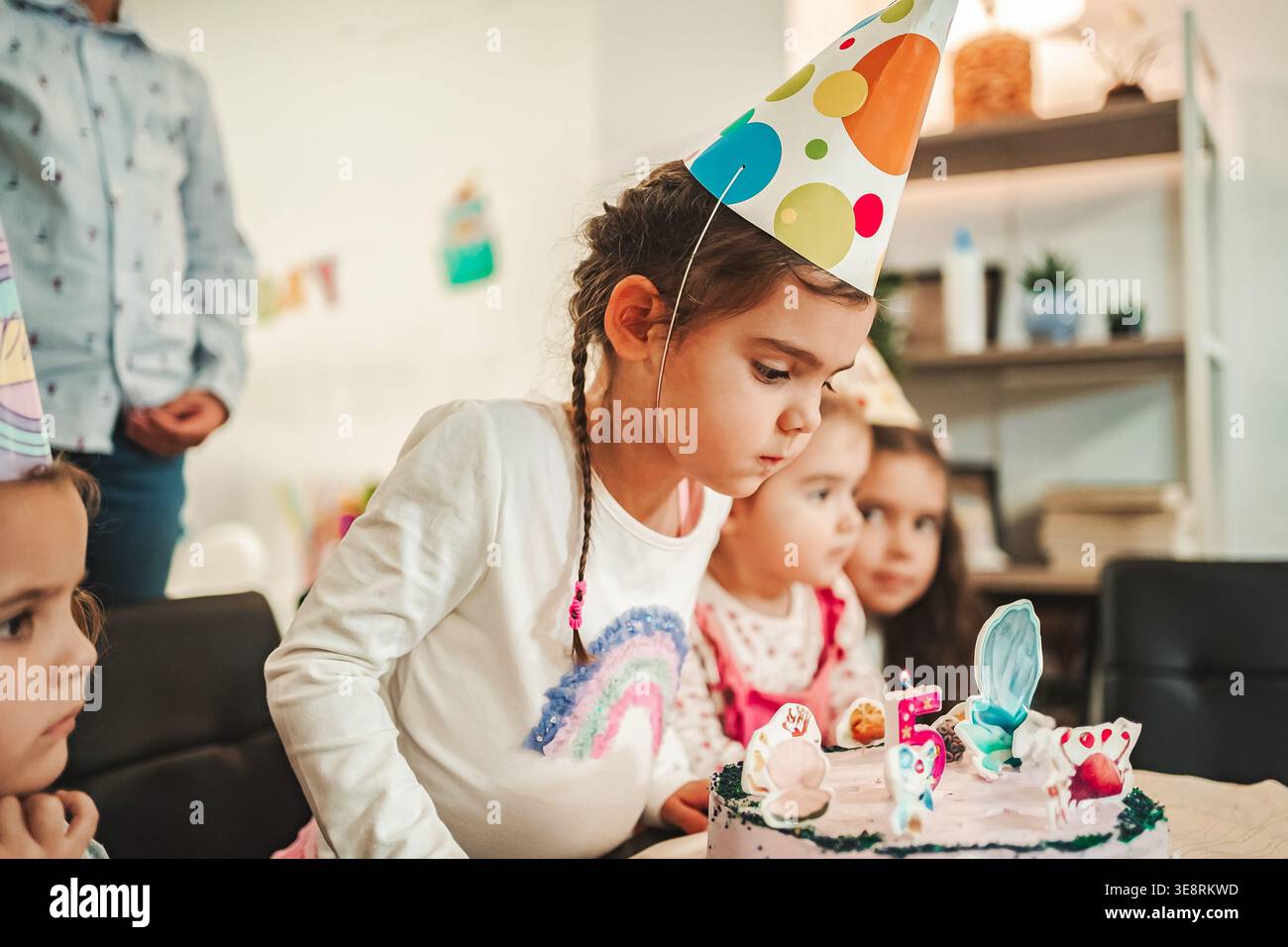 Children celebrate a birthday with a cake and party hats in a room with ...