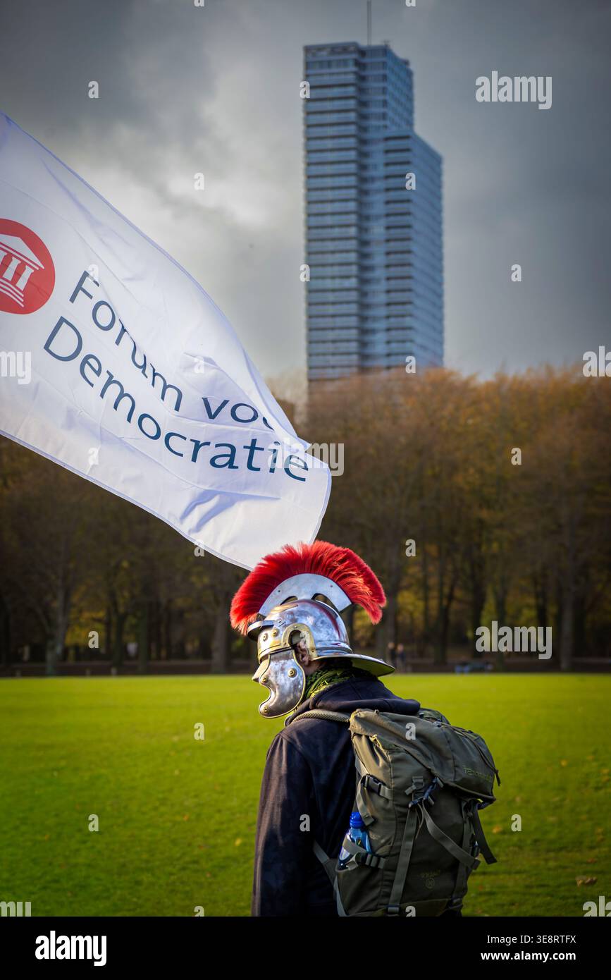 November 7, 2021, Malieveld, The Hague, Netherlands: A man wearing a Roman-style helmet and backpack walks on the grass beside a “Forum voor Democrati Stock Photo