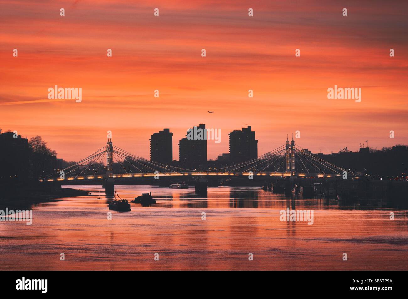 View of the famous Albert Bridge spanning the River Thames with World's End Estate silhouette as seen from Chelsea Bridge at sunset. London UK sunsets Stock Photo