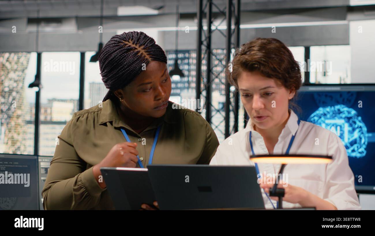 Programmers in office automating workflows using artificial intelligence technology. Teamworking colleagues refining deep learning computational models for faster processing, camera B Stock Photo