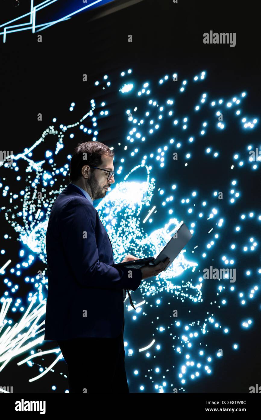 Technician monitors deep learning AI model patterns using laptop. RD lab employee studies artificial intelligence neural network algorithm nodes on digital wall to understand processing using notebook Stock Photo