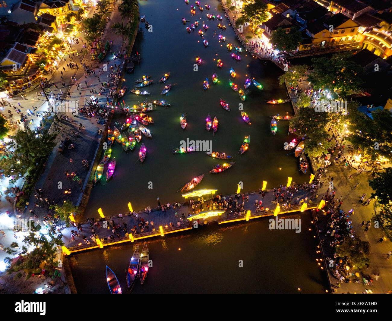 Aerial view of traditional wooden boats with colorful lanterns on the river at night with people on the bridge and illuminated buildings in Hoi An, Vi Stock Photo