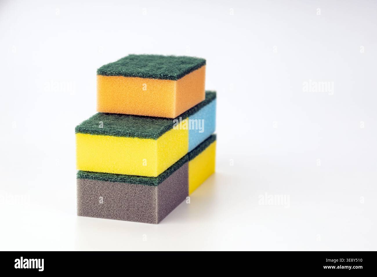 Stack of three colorful kitchen cleaning sponges with bright yellow, warm orange, and gray foam cores, each topped with dark green abrasive scrubbing Stock Photo