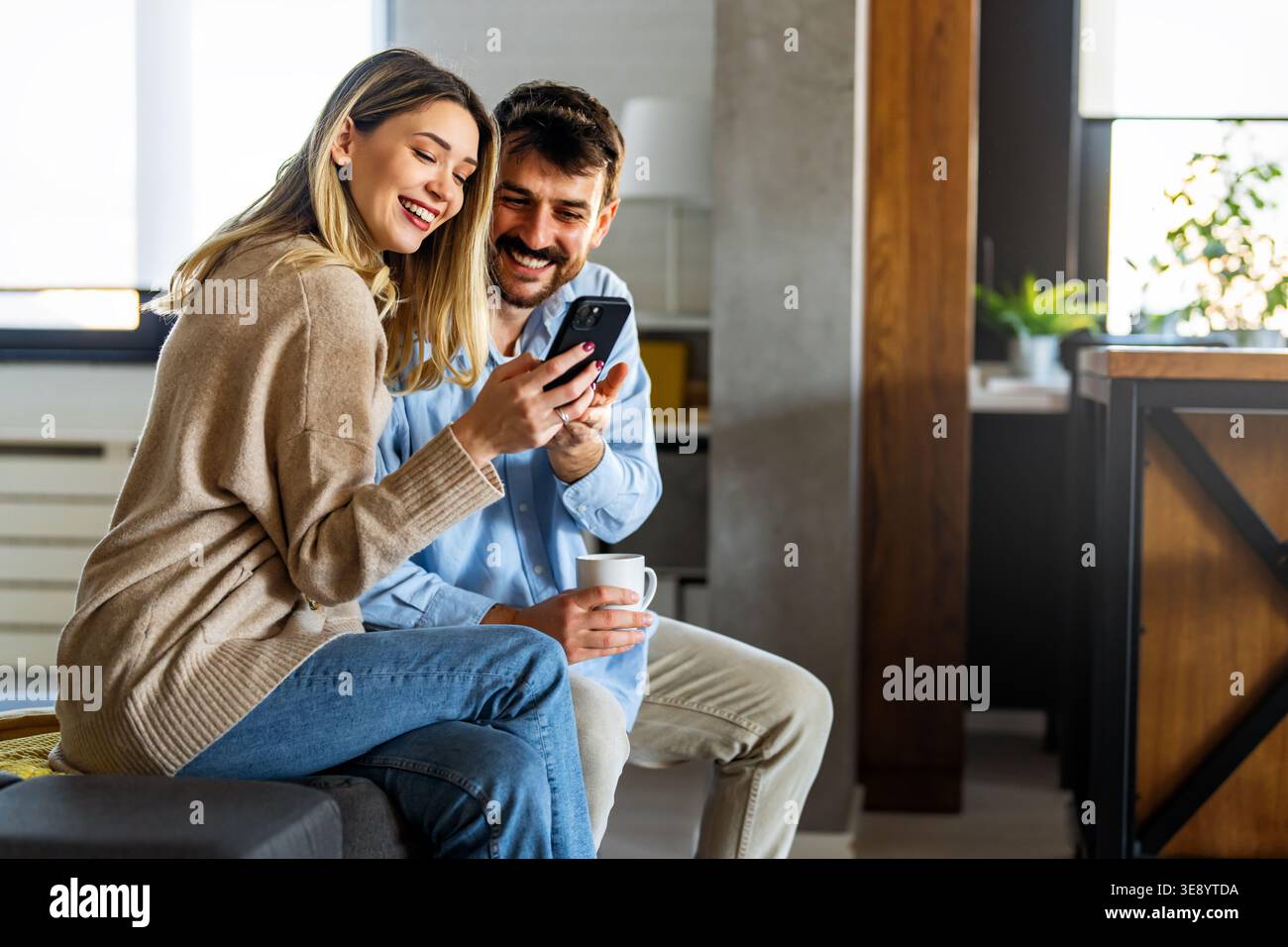 Young happy multiethnic couple having fun while using laptop, digital device at home Stock Photo