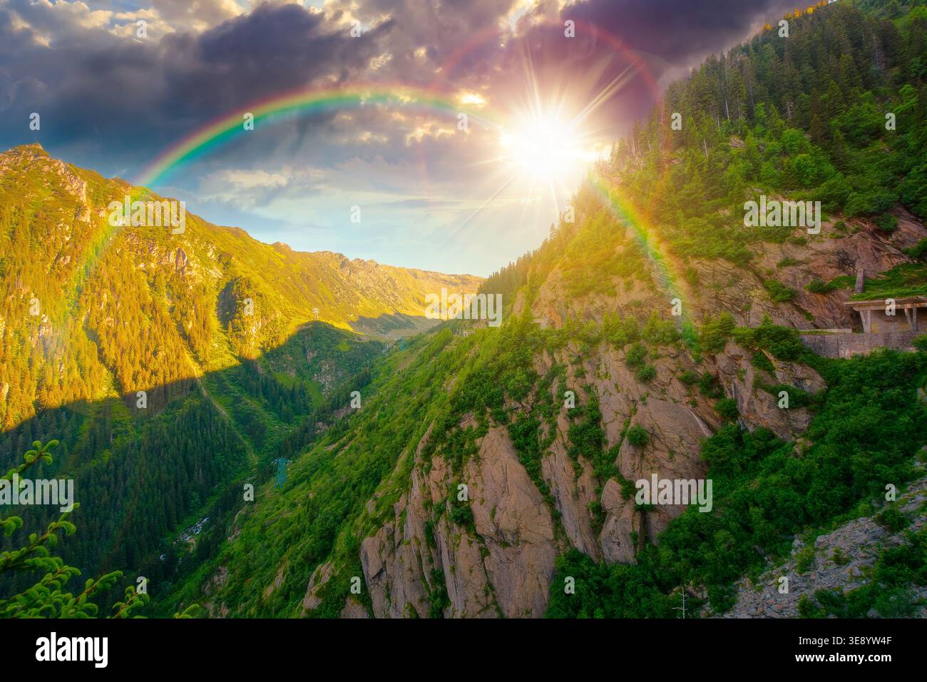 sunset over valley in summer mountains. Gorgeous mountainous landscape. Rocky cliffs and forested slopes under cloudy sky. Scenery of mountain ridge i Stock Photo