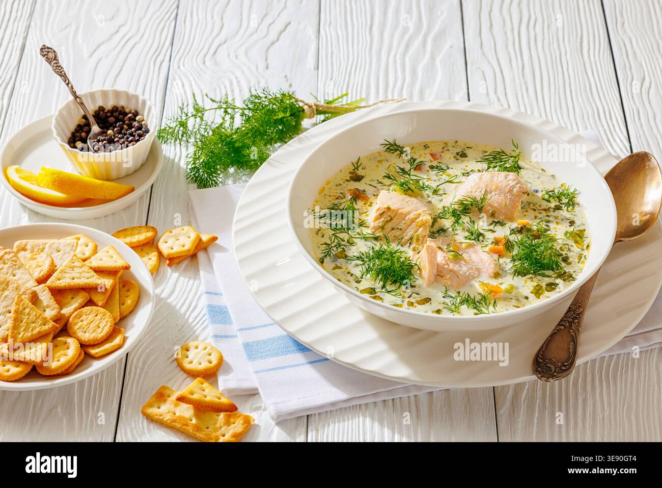 A bowl of traditional Nordic lohikeitto or laxsoppa creamy salmon soup with chunks of fish and fresh dill served with crackers, lemon slices and peppe Stock Photo