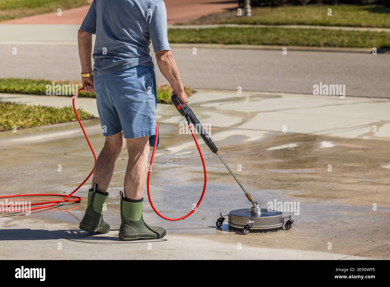 Man using pressure washer surface cleaner to power wash residential concrete driveway sidewalk. Stock Photo