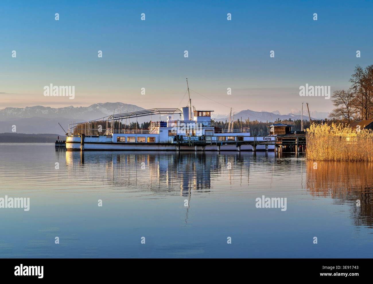 Altes stillgelegtes Ausflugsschiff an einem Holzsteg spiegelt sich im klaren Wasser im Morgenlicht am Starnberger See, Tutzing, Bayern, Deutschland Eu Stock Photo