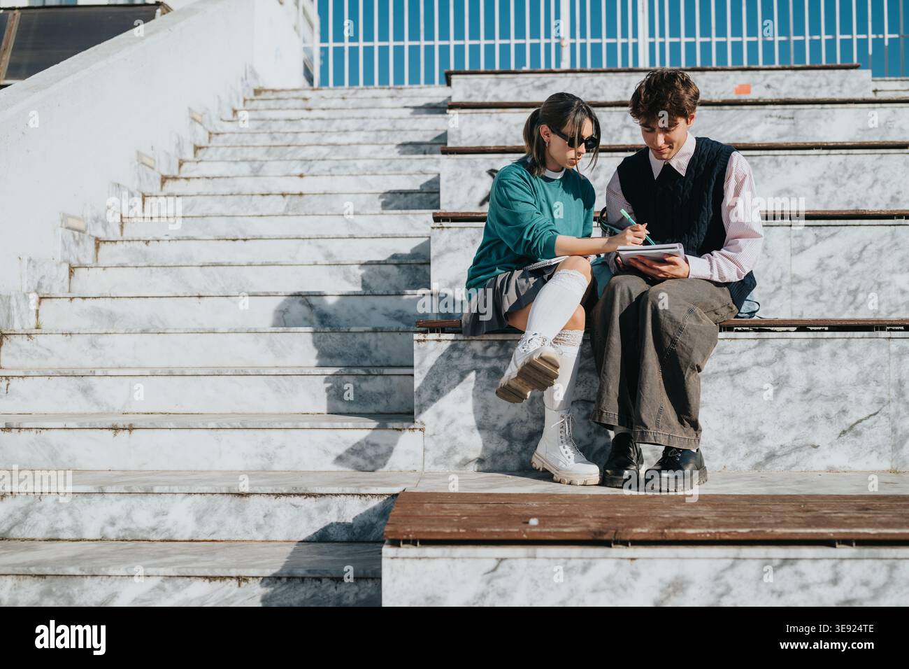 Two students studying together on marble stadium steps, collaborating and taking notes outdoors Stock Photo
