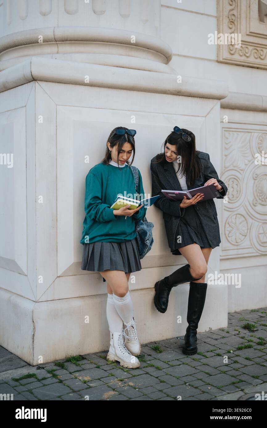 Two students studying together outside a classical building, reading notebooks and talking Stock Photo