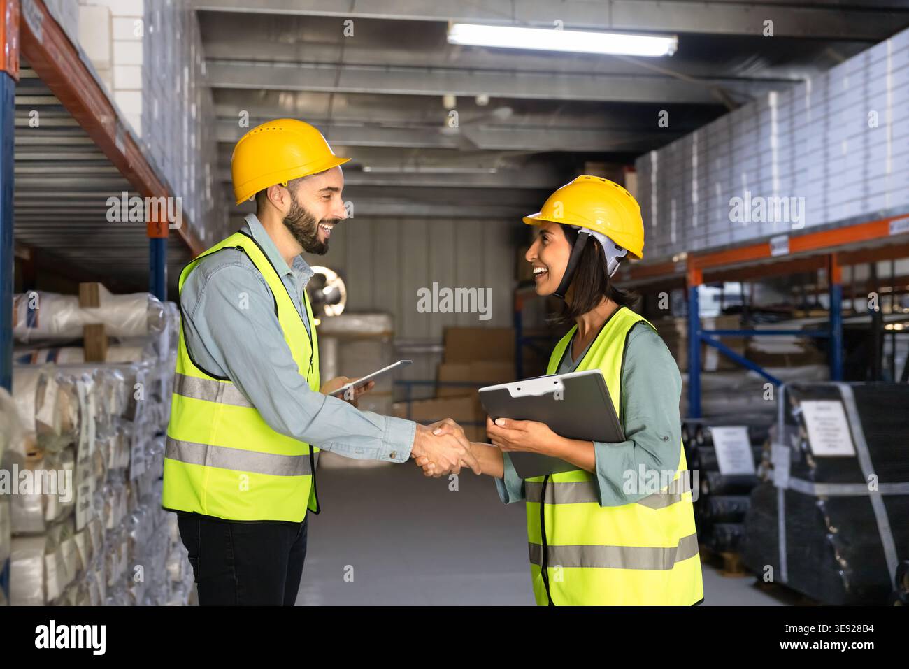 Warehouse workers shaking hands in storehouse aisle Stock Photo