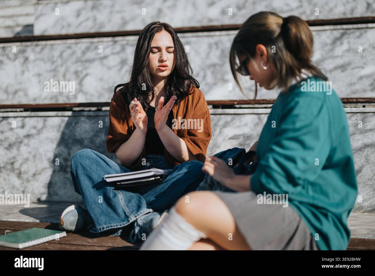 Two young women studying and discussing notes while sitting outdoors on steps Stock Photo