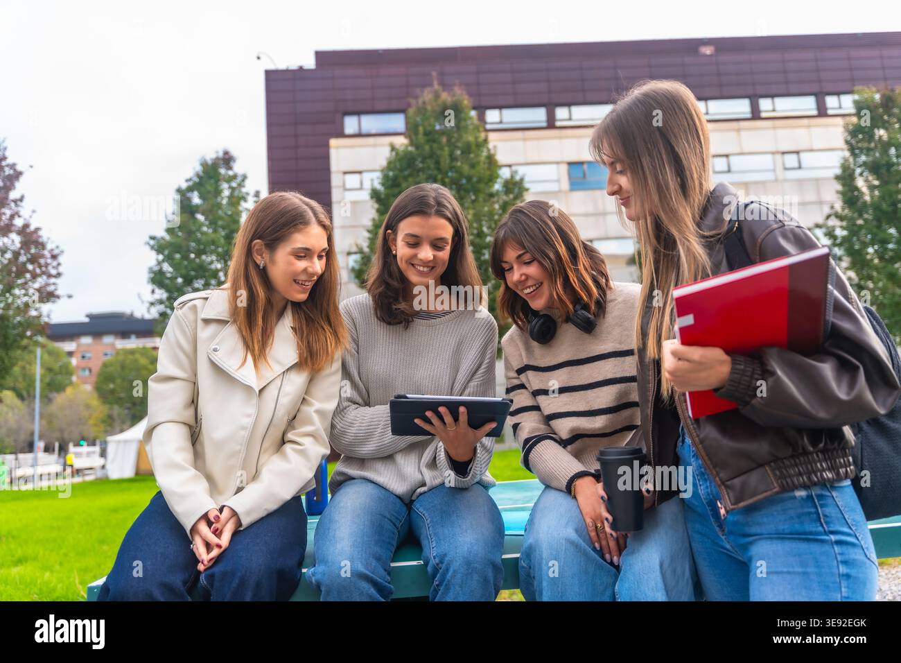 Students group sitting outdoors using tablet on campus Stock Photo