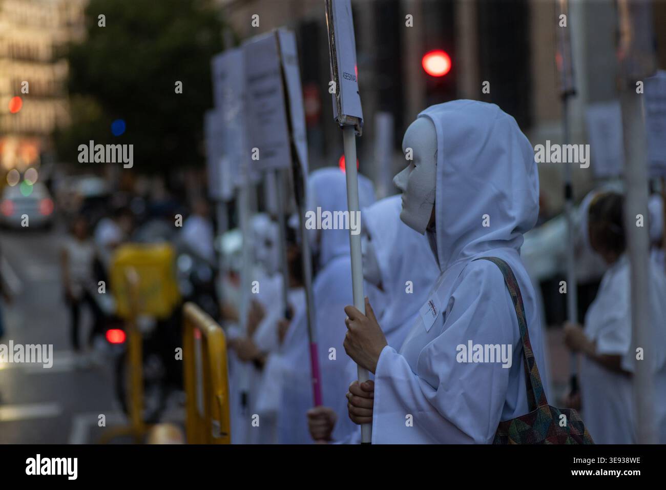 A woman wearing a white robe and mask participates in a demonstration ...