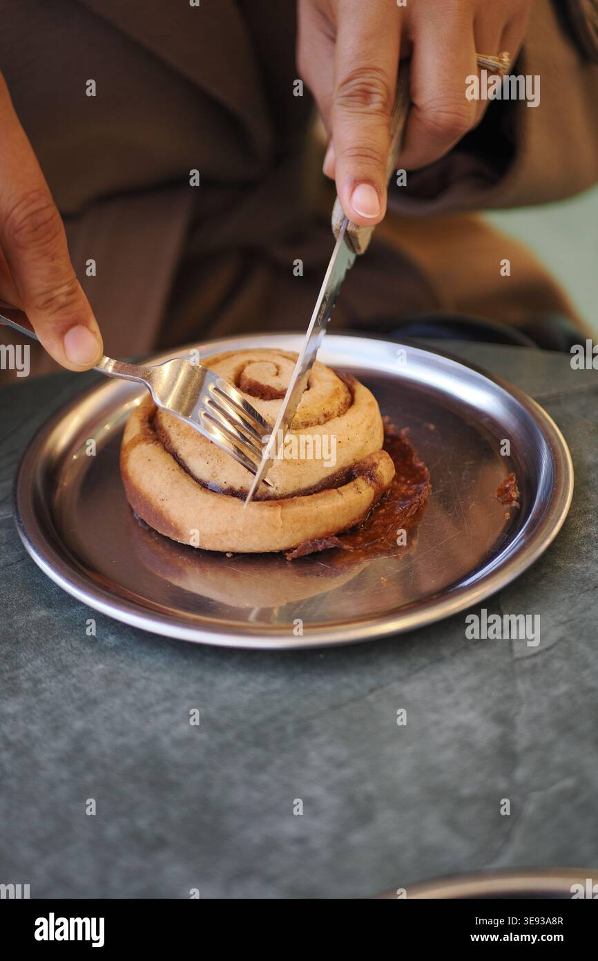 Cutting a cinnamon roll on a metal plate Stock Photo
