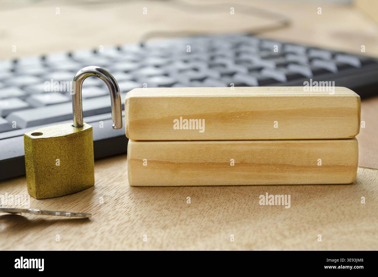 A bright brass padlock positioned on a desk near a computer keyboard with blank wooden blocks with customizable space for text Stock Photo