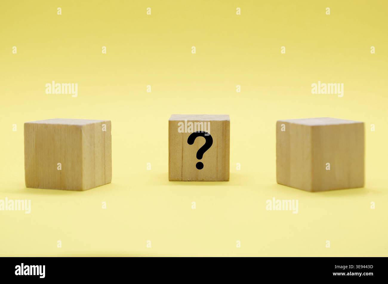 Three light wooden blocks with question marks on pale surface with yellow backdrop Stock Photo
