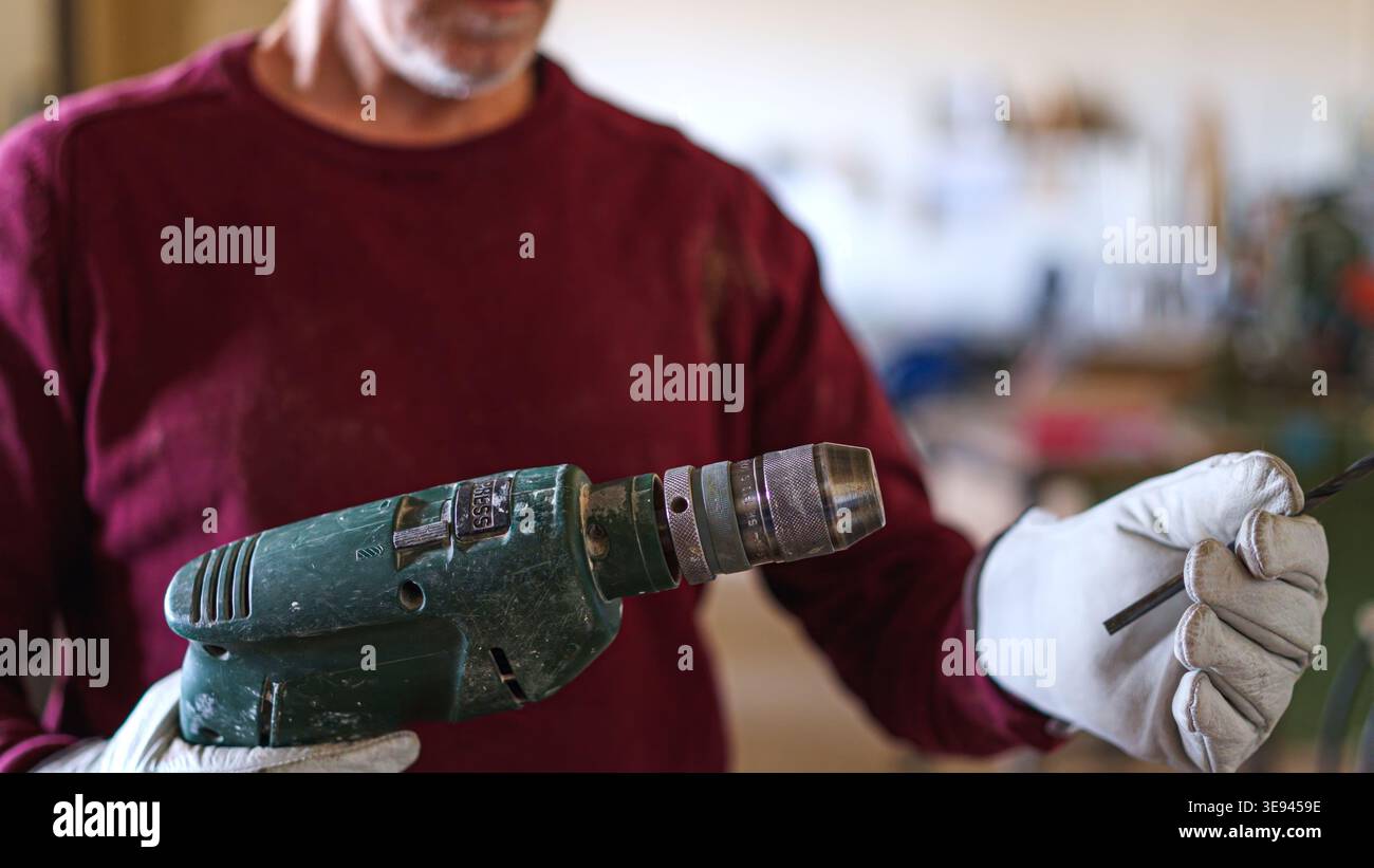 Artisan wearing gloves inserting drill bit into power tool Stock Photo