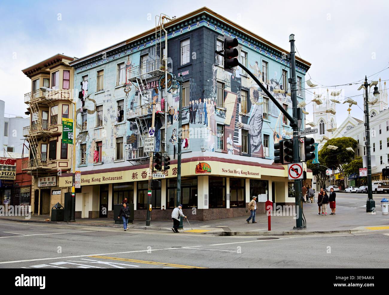 Visitors walk past colorful murals on buildings in Chinatown, San Francisco, capturing local culture and art in the busy streets. Stock Photo