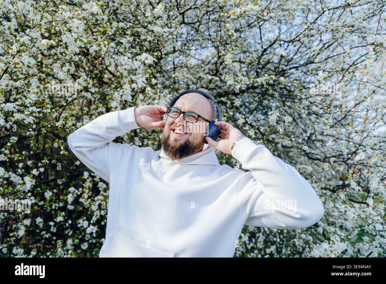Happy kind bearded man wearing headphones near blooming tree in spring Stock Photo