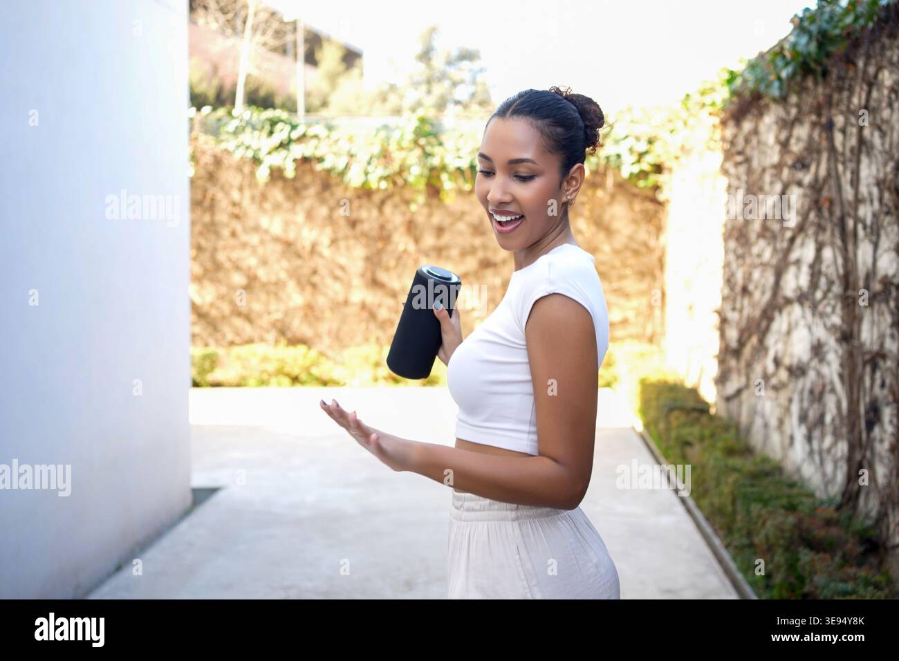 Energized entrepreneur in white dress excitedly sharing product details in lush courtyard setting Stock Photo