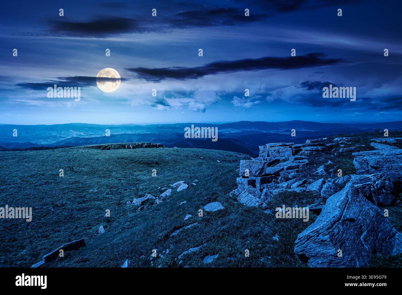 mountainous landscape during summertime at night. full moon over boulders and rock formations surrounded grassy hills. picture of an untouched highlan Stock Photo