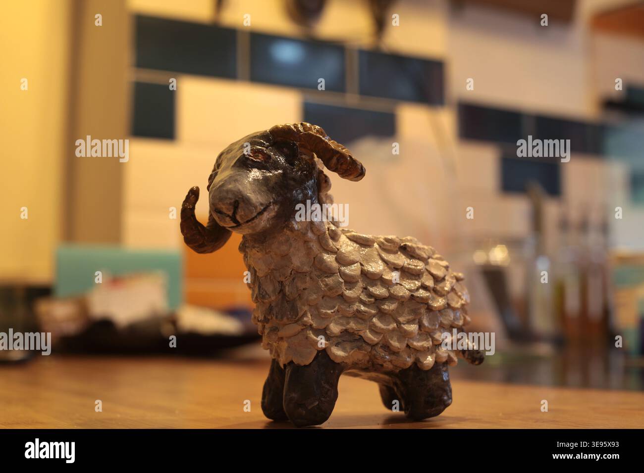 Handmade ceramic sheep ram figurine with curled horns on a wooden table in cozy cafe, shallow depth of field and warm indoor lighting. The Ram, 'rammi Stock Photo