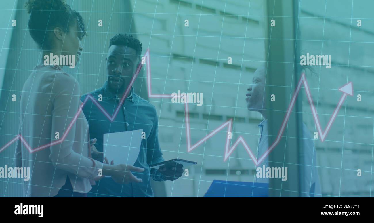 Analyzing line chart overlay, three colleagues in business wear discussing tablet, data in atrium Stock Photo